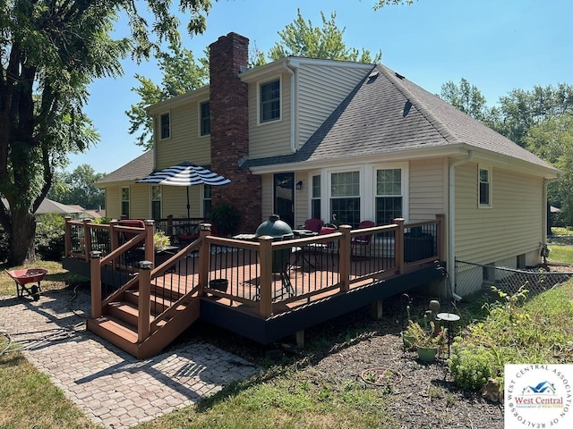 back of house with a chimney, roof with shingles, fence, a deck, and outdoor dining space