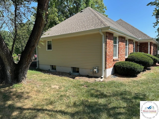 view of home's exterior featuring brick siding, roof with shingles, and a yard