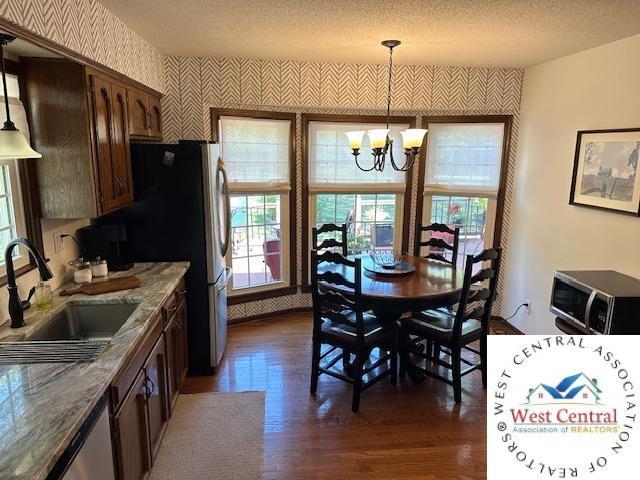 dining space featuring dark wood-style floors, a textured ceiling, an inviting chandelier, and wallpapered walls