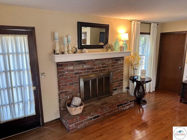 living room featuring a textured ceiling, a brick fireplace, wood finished floors, and baseboards