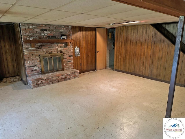 finished below grade area featuring light floors, wood walls, a fireplace, and a paneled ceiling