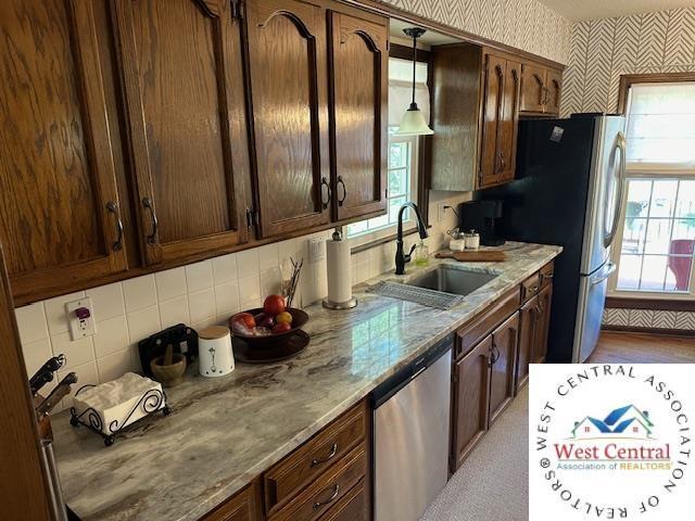 kitchen with light stone counters, decorative light fixtures, stainless steel appliances, a sink, and wallpapered walls