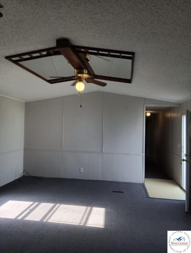 empty room featuring vaulted ceiling, dark carpet, and a textured ceiling