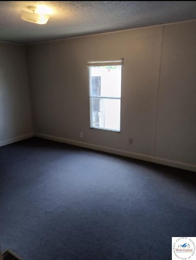 unfurnished room with a textured ceiling, dark carpet, and baseboards