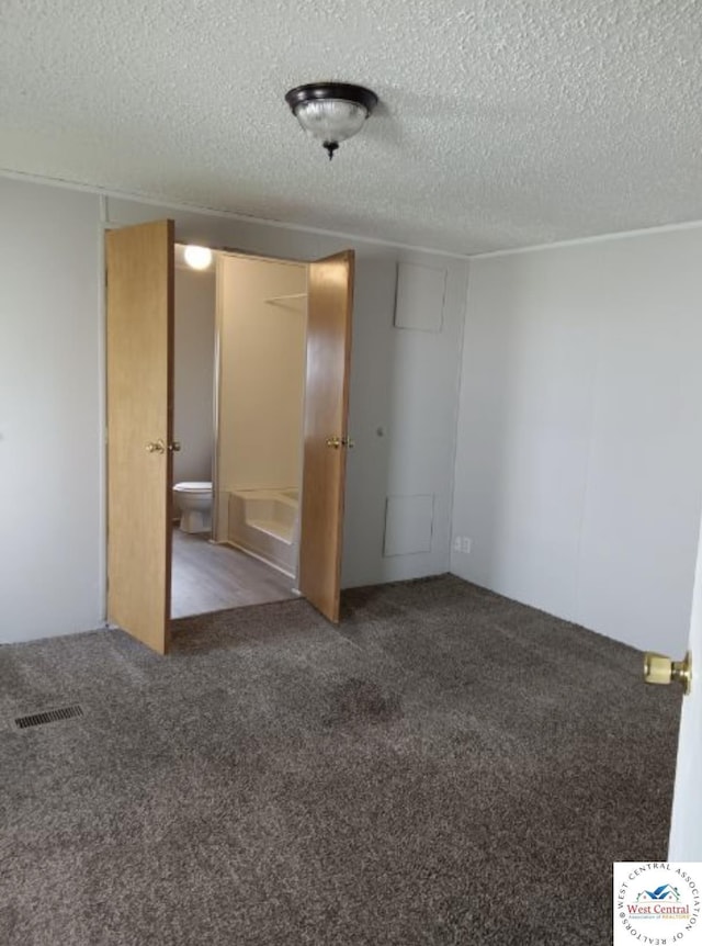 spare room with visible vents, dark carpet, and a textured ceiling