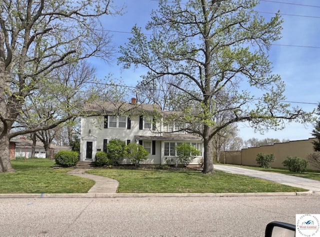 view of front of house featuring driveway, a chimney, fence, and a front lawn