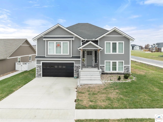 bi-level home with concrete driveway, stone siding, roof with shingles, an attached garage, and a front lawn