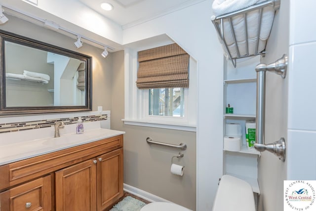 half bath featuring toilet, track lighting, tasteful backsplash, baseboards, and vanity