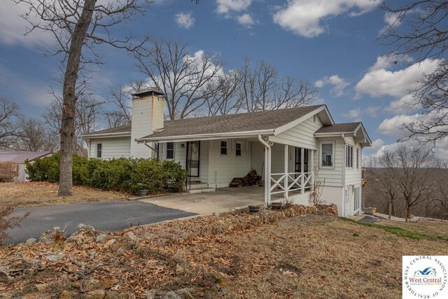 single story home featuring covered porch, a chimney, and driveway