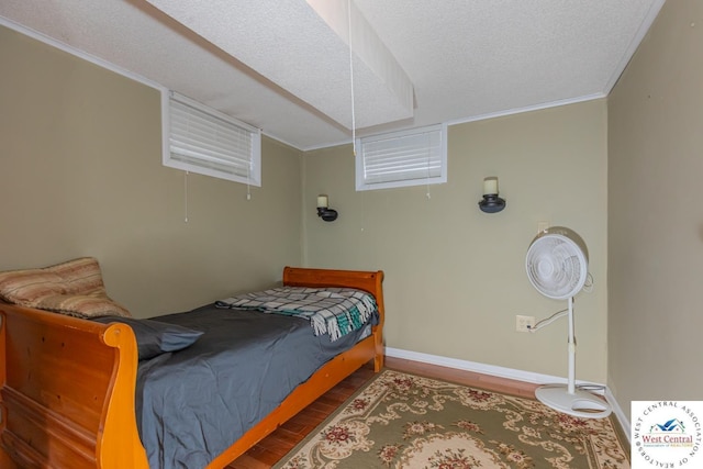 bedroom featuring a textured ceiling, crown molding, baseboards, and wood finished floors