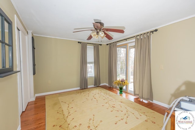 interior space featuring a ceiling fan, crown molding, wood finished floors, and baseboards