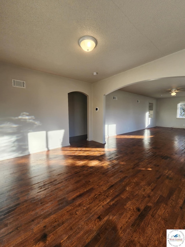 empty room featuring arched walkways, ceiling fan, a textured ceiling, visible vents, and dark wood-style floors