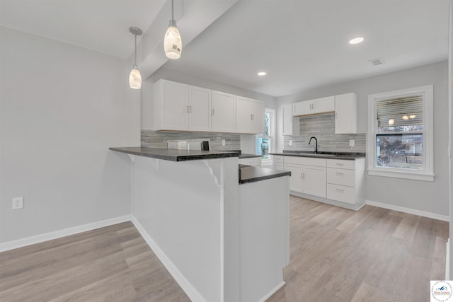 kitchen featuring light wood-type flooring, dark countertops, a sink, and a peninsula