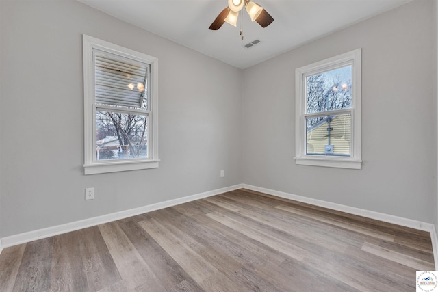 unfurnished room featuring plenty of natural light, wood finished floors, visible vents, and baseboards