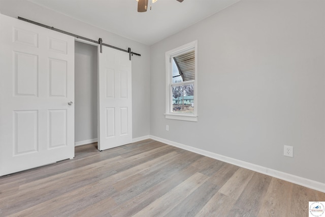 unfurnished bedroom with a ceiling fan, a barn door, baseboards, and wood finished floors