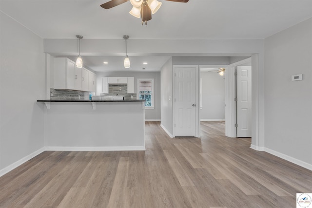 kitchen with a peninsula, white cabinetry, light wood-type flooring, backsplash, and dark countertops