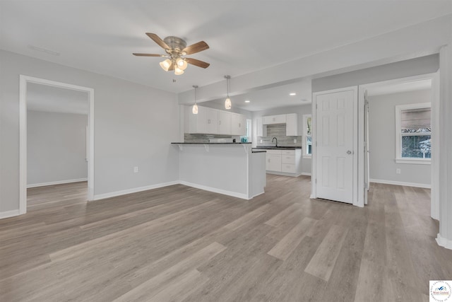 kitchen featuring light wood finished floors, tasteful backsplash, white cabinets, dark countertops, and a peninsula