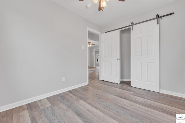 unfurnished bedroom featuring a ceiling fan, a barn door, baseboards, and wood finished floors