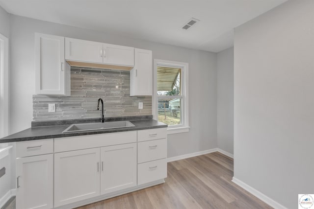 kitchen with white cabinets, light wood-style flooring, backsplash, and a sink