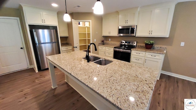 kitchen with an island with sink, appliances with stainless steel finishes, light stone countertops, pendant lighting, and a sink