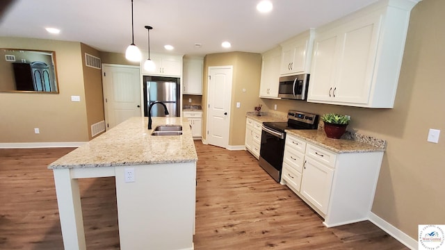 kitchen with visible vents, hanging light fixtures, appliances with stainless steel finishes, a kitchen island with sink, and light stone countertops