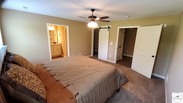 bedroom with dark colored carpet, visible vents, a barn door, ensuite bath, and baseboards