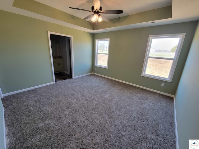 unfurnished bedroom featuring visible vents, baseboards, a raised ceiling, ensuite bathroom, and dark carpet