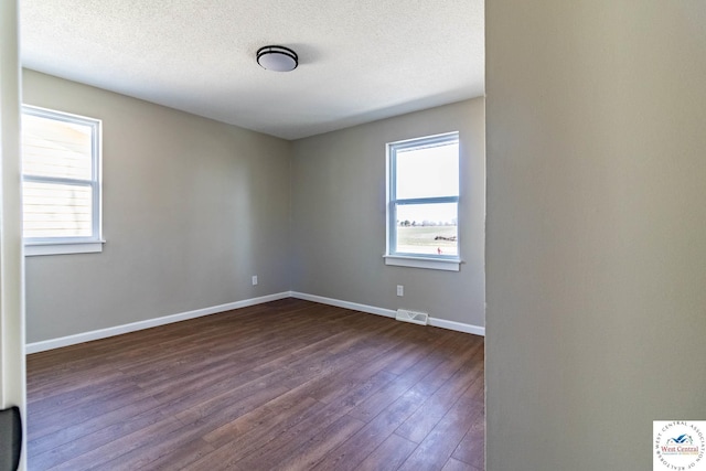 unfurnished room featuring visible vents, baseboards, a textured ceiling, and dark wood finished floors