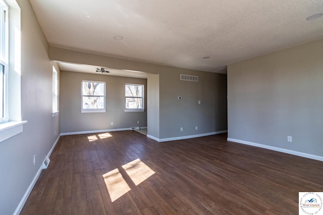 empty room featuring visible vents, baseboards, a textured ceiling, and dark wood-style flooring