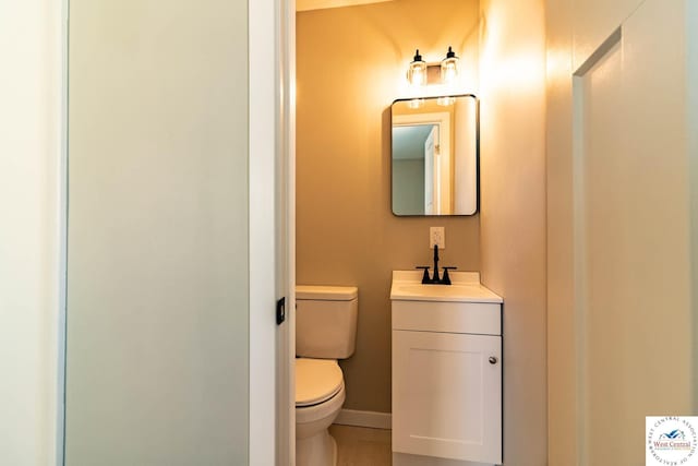 half bathroom with baseboards, toilet, and vanity