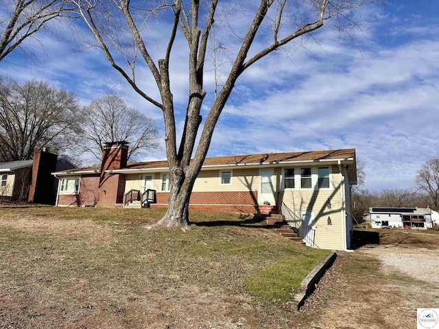 rear view of property with entry steps, brick siding, a chimney, and a lawn