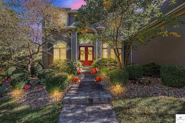 exterior entry at dusk featuring french doors and stucco siding