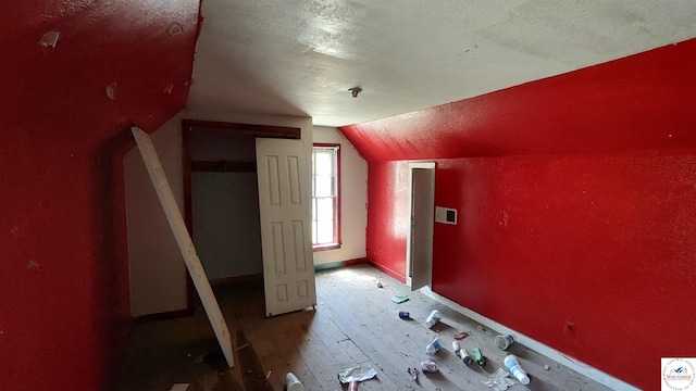 additional living space featuring a textured ceiling, wood finished floors, lofted ceiling, and visible vents