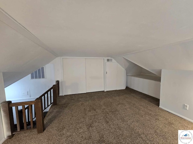 additional living space featuring lofted ceiling, dark colored carpet, and visible vents