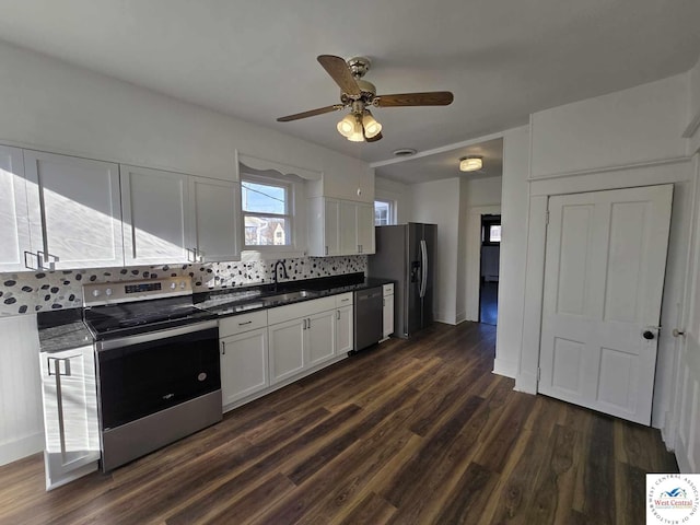 kitchen featuring tasteful backsplash, white cabinets, dark countertops, stainless steel appliances, and a sink