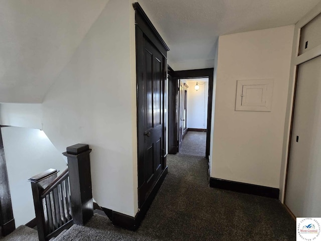 hall with baseboards, dark carpet, and an upstairs landing