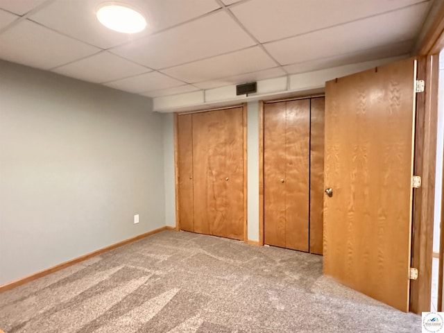 unfurnished bedroom with a paneled ceiling, baseboards, carpet floors, and multiple closets