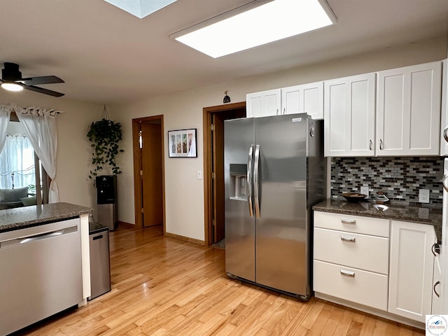 kitchen featuring backsplash, appliances with stainless steel finishes, light wood-style floors, white cabinetry, and dark stone counters