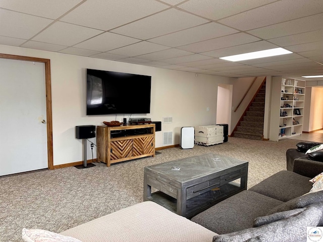 carpeted living area with a drop ceiling, stairway, and baseboards