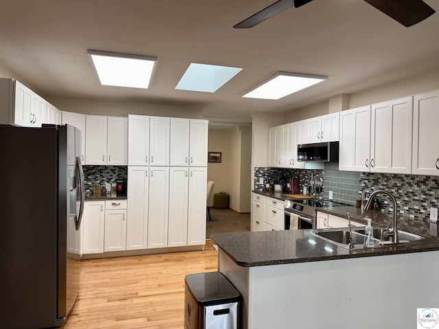 kitchen featuring appliances with stainless steel finishes, white cabinetry, a sink, and a peninsula
