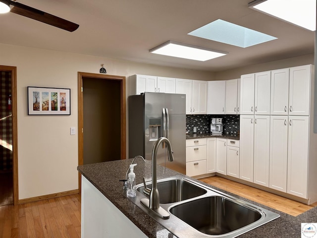 kitchen with stainless steel fridge, tasteful backsplash, white cabinets, light wood-type flooring, and a sink