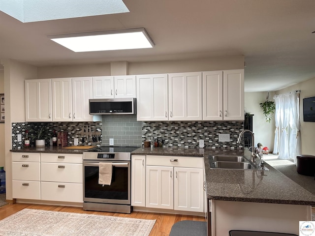 kitchen featuring light wood finished floors, tasteful backsplash, appliances with stainless steel finishes, white cabinets, and a sink