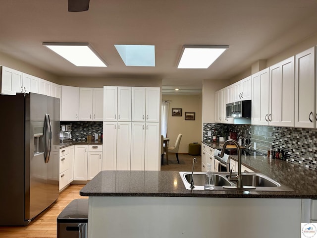 kitchen with stainless steel appliances, a peninsula, a sink, and white cabinets