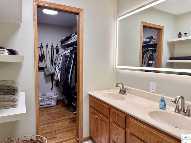 full bathroom featuring double vanity, a walk in closet, a sink, and wood finished floors
