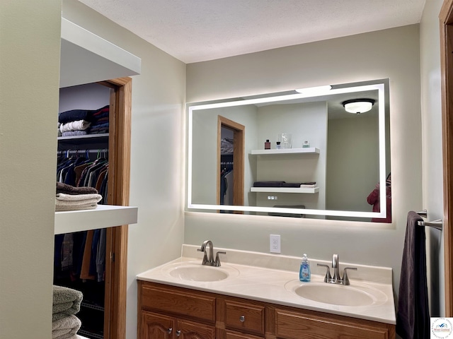 full bathroom with double vanity, a textured ceiling, a spacious closet, and a sink