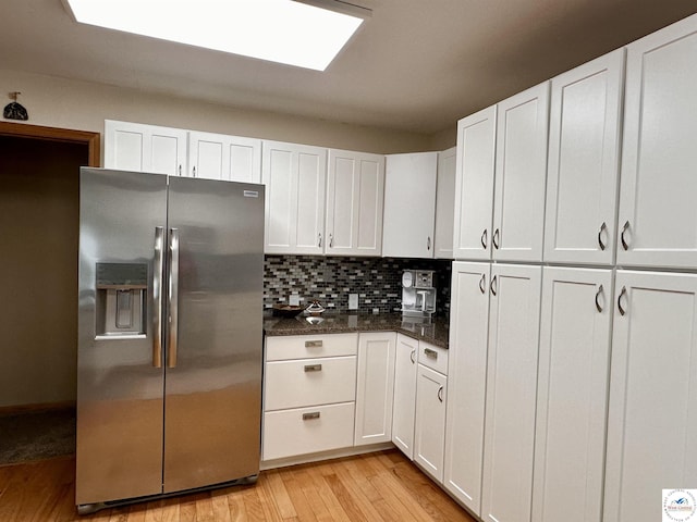 kitchen with a skylight, white cabinetry, light wood-type flooring, decorative backsplash, and stainless steel fridge