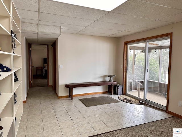 doorway to outside with light tile patterned flooring, a paneled ceiling, and baseboards