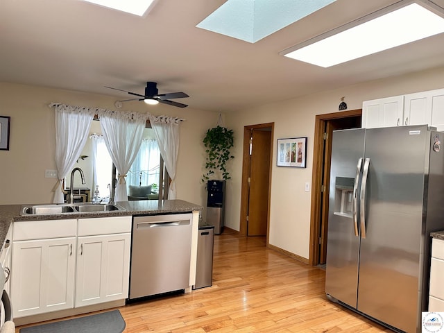 kitchen with light wood-style flooring, a sink, white cabinets, appliances with stainless steel finishes, and dark stone counters