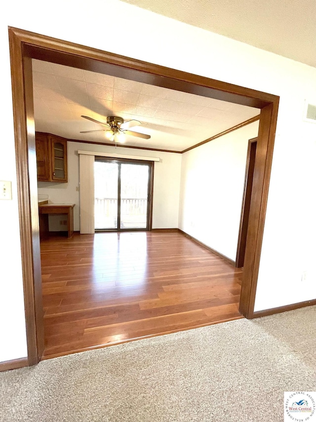 spare room with ceiling fan, wood finished floors, carpet flooring, baseboards, and crown molding