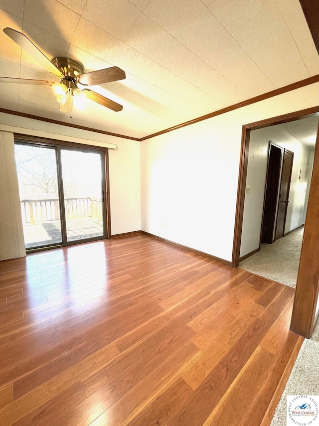 empty room with ceiling fan, baseboards, crown molding, and wood finished floors